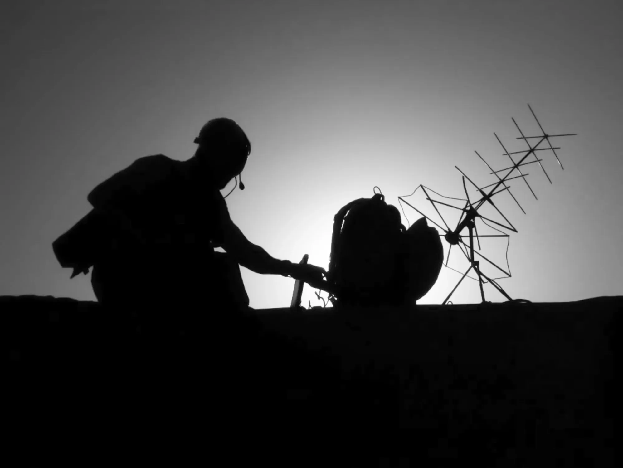 Operator with a headset at field communications equipment, silhouetted against the sky