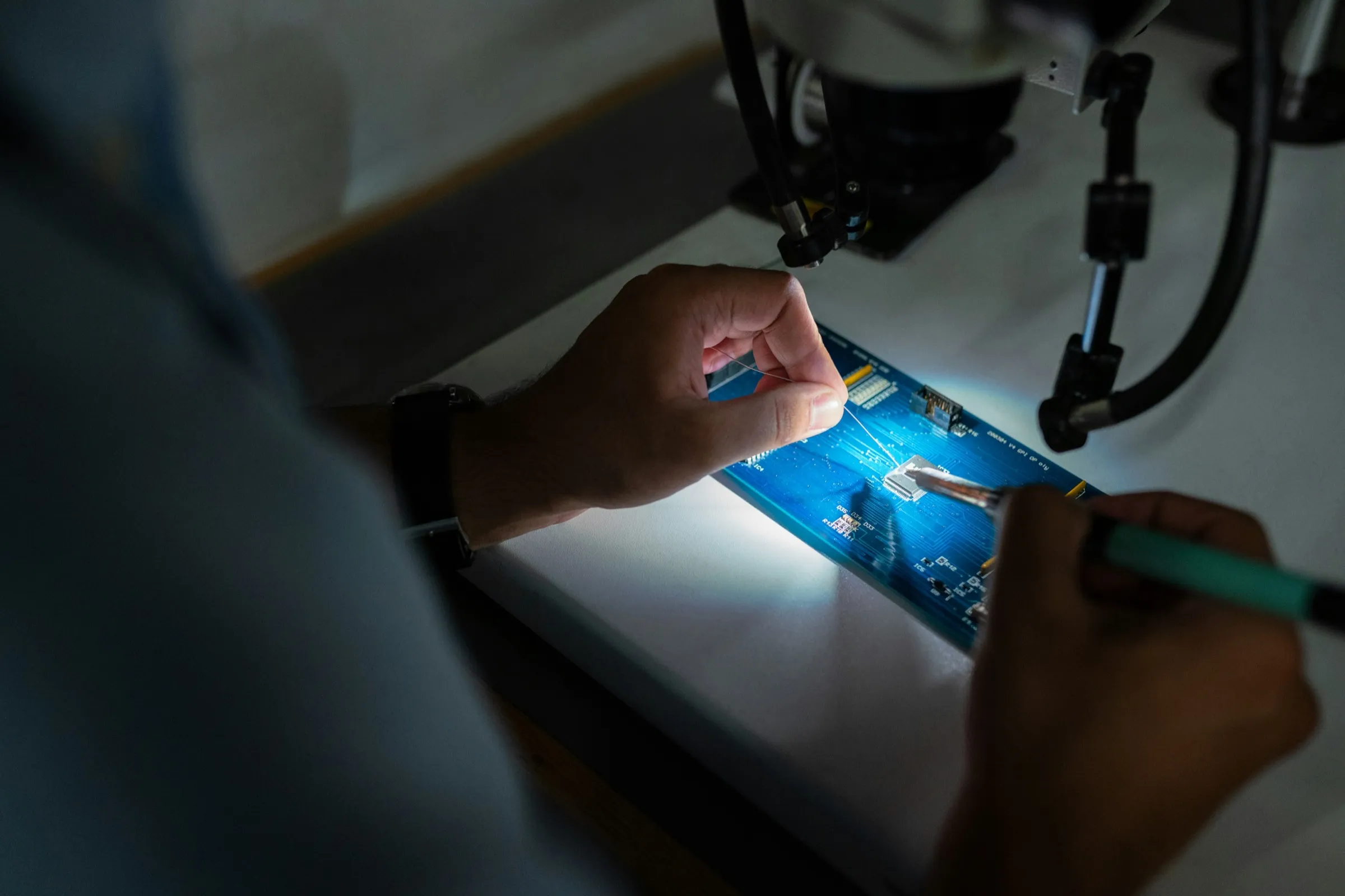 Hands soldering a circuit board under a work lamp